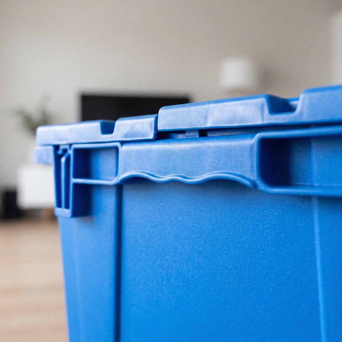Close-up of the secure attached lid latch on a blue reusable plastic moving crate available to rent in Fort Smith AR